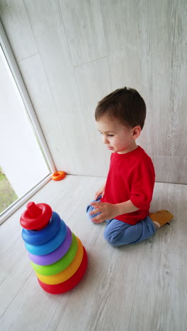 cute caucasian baby boy sits on the floor building a pyramid. peaceful game of a toddler at home. vertical video.