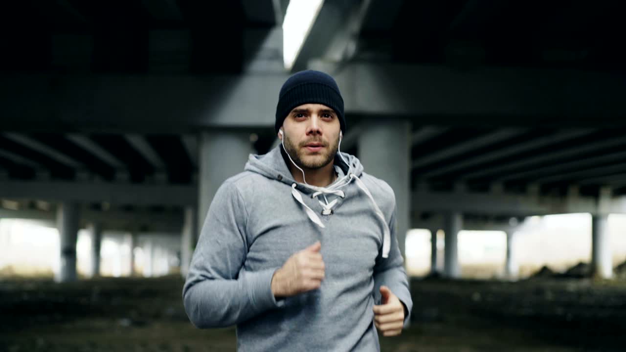 Tracking shot of sportive man runner putting on earphones and starts running at urban outdoors city location in winter