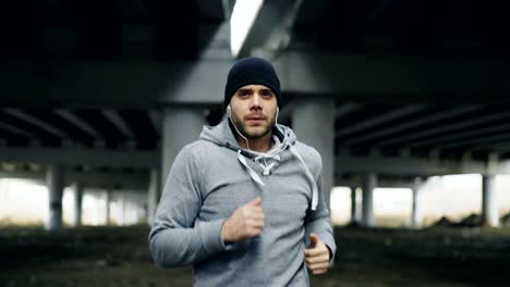 tracking shot of sportive man runner putting on earphones and starts running at urban outdoors city location in winter