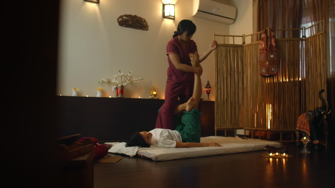 Thai massage salon. Asian woman in traditional clothes doing therapeutic relaxing massage Caucasian woman. Professional traditional massage. Alternative medicine.