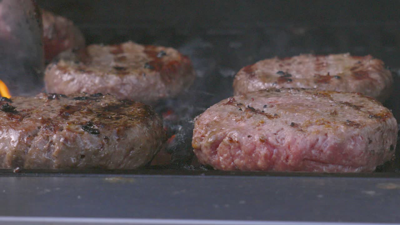 Collection of Juicy Beef Burgers on Flame Grill BBQ with Welldone and Medium Rare Patties. High Quality Outdoor Summer Cooking Footage. Spatula Used to Flip Meat.