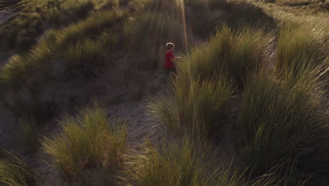 drone shot of young boy on beach vacation playing in sand dunes against flaring sun