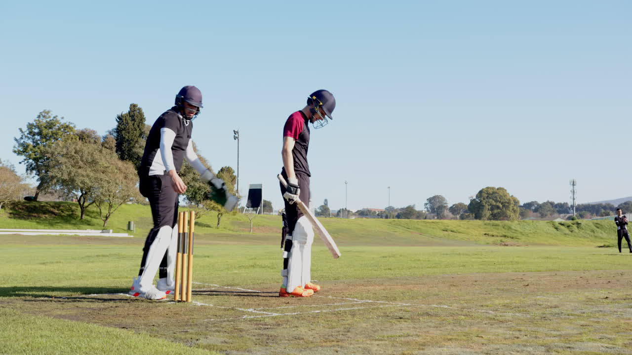 Cricket players preparing on field, adjusting gear under sunny sky