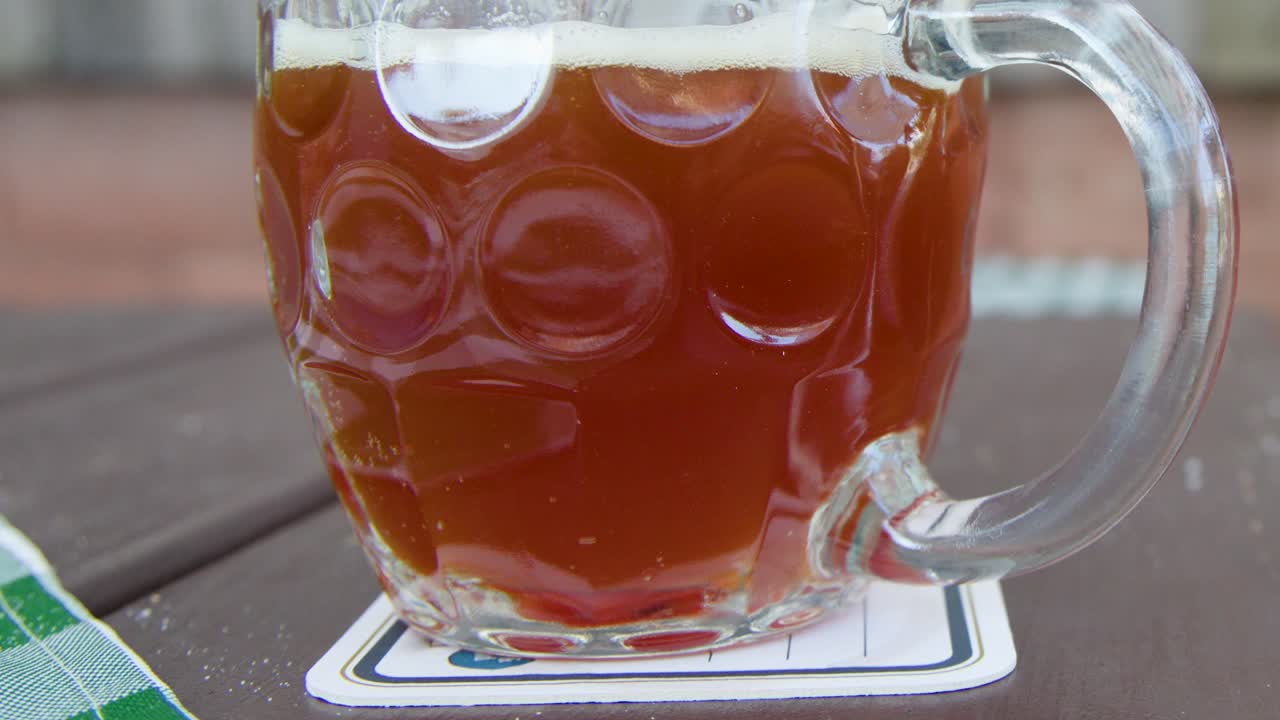 A hand lifts a traditional beer mug from a wooden table in natural daylight