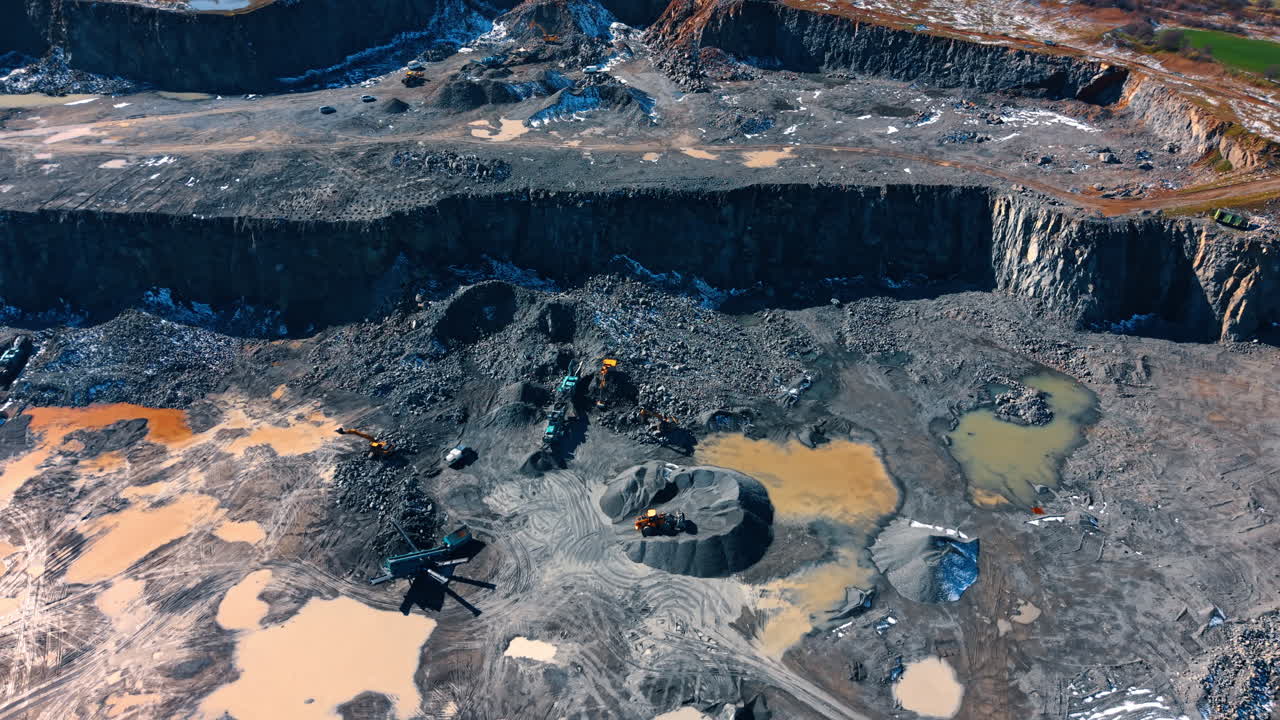Aerial view of stone crushing equipment in quarry pit. Mobile crushers and excavators processing piles of granite rock on the floor of an open-cast mine