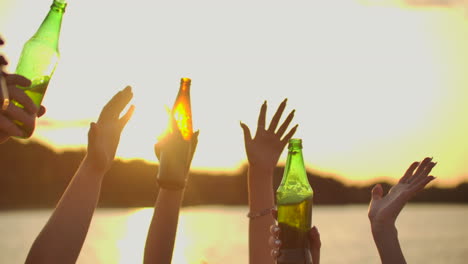 company of young students are dancing with hands up with beer. this is perfect party at sunset on the lake coast.