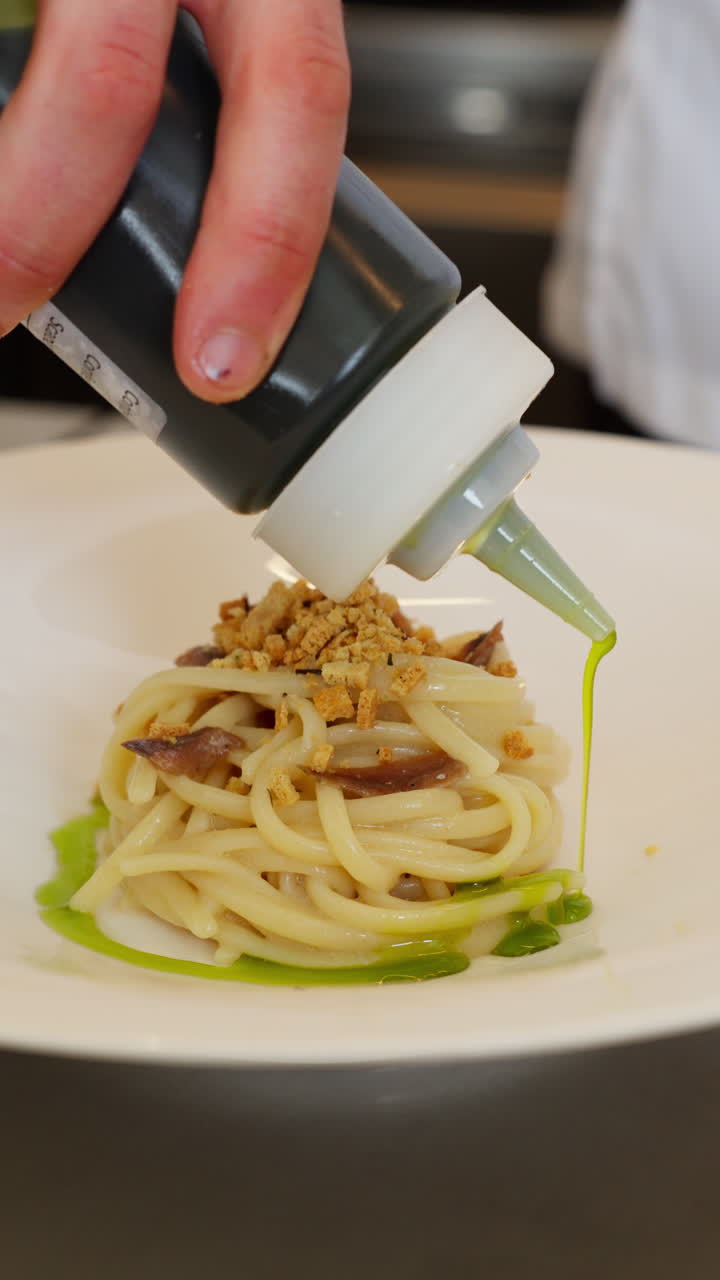 Chef che impiattano spaghetti gourmet con salsa verde e pangrattato