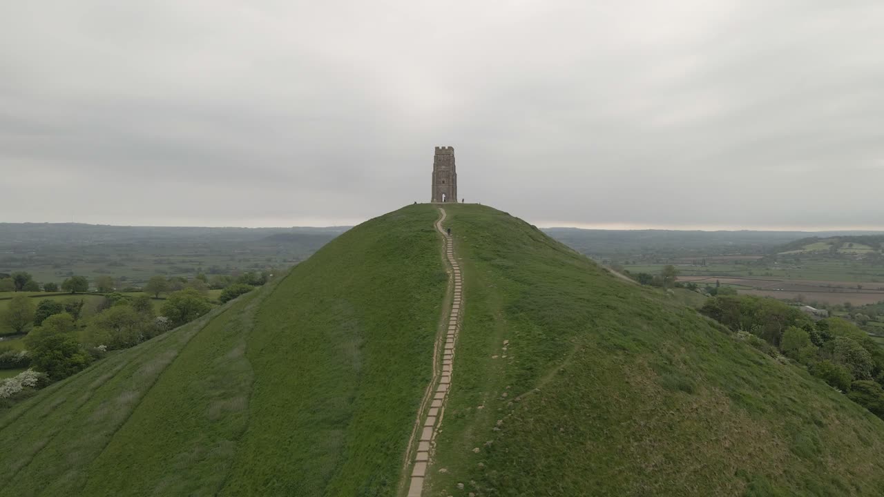 Aerial view of Glastonbury, drone moving forward towards the St Michaels tower, drone flying over the green fields. 4K, 60fps.