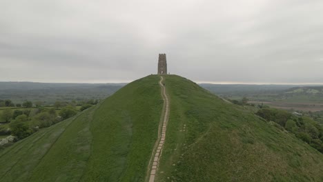 aerial view of glastonbury, drone moving forward towards the st michaels tower, drone flying over the green fields. 4k, 60fps.