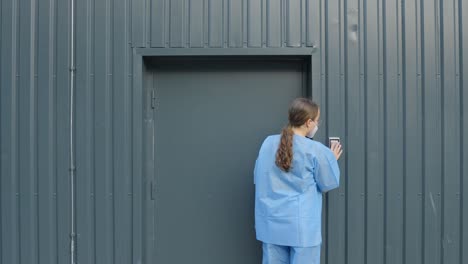 Woman-wearing-blue-coat-walks-towards-the-security-door-and-enters-her-passcode-to-get-in,-static