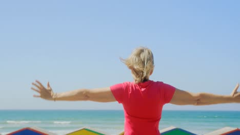 rear view of active senior caucasian woman standing with arms outstretched on promenade at beach 4k