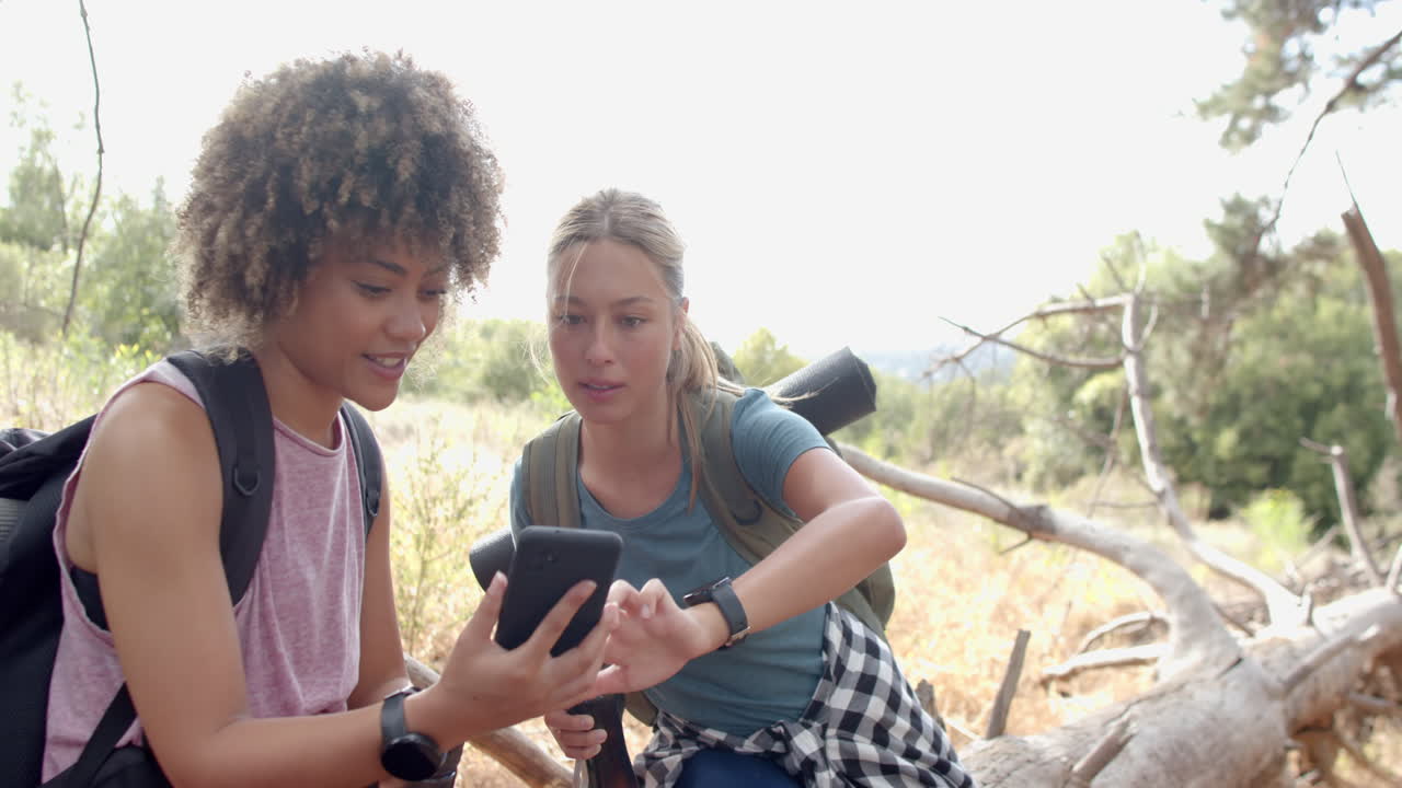 Two women are examining a smartphone during a hike in the woods