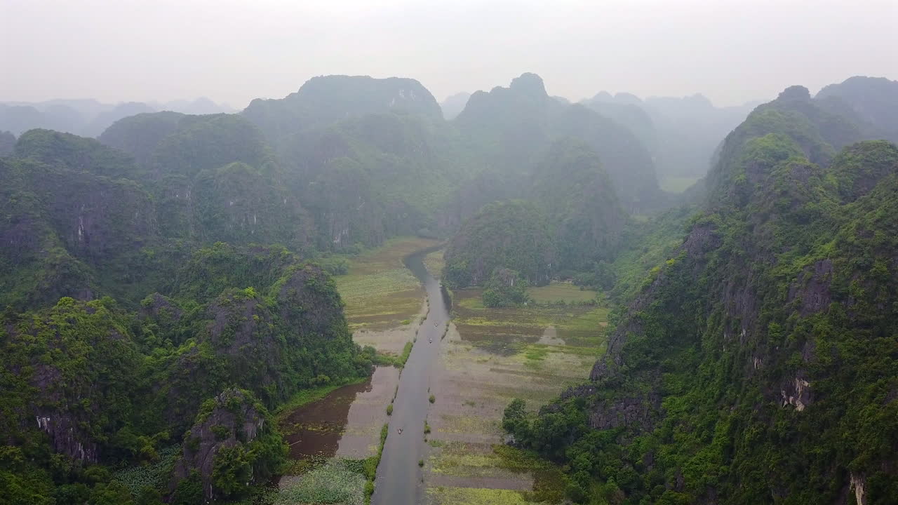 Experience the atmospheric front view of a road winding through the majestic, rain-kissed mountains of Ninh Binh, Vietnam on a cloudy day. Discover the unique beauty of this region.