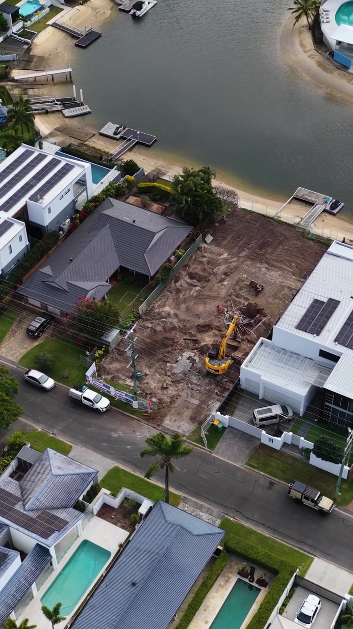 High-angle drone shot of an excavator working on a residential lot near luxury canals.
