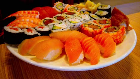 sushi-rolls-maki-assorted-round-white-plate-rotating-on-wooden-table-in-restaurant-where-shadows-of-people-walking-by-in-the-background