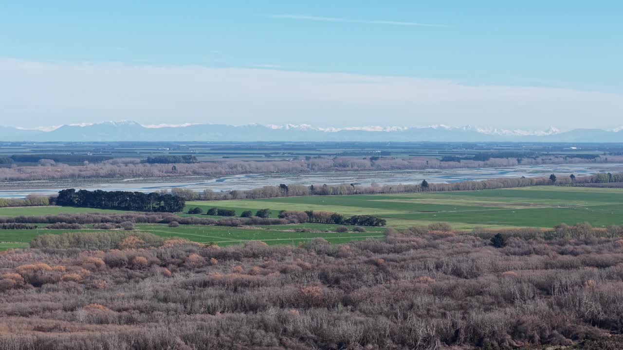 Flying sideways above lagoon with zoomed in view of lush farmland, braided Rakaia River and foothills of the Southern Alps (Canterbury, New Zealand)
