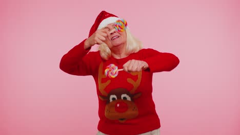 senior grandmother in christmas sweater holding candy striped lollipops, dancing making silly faces