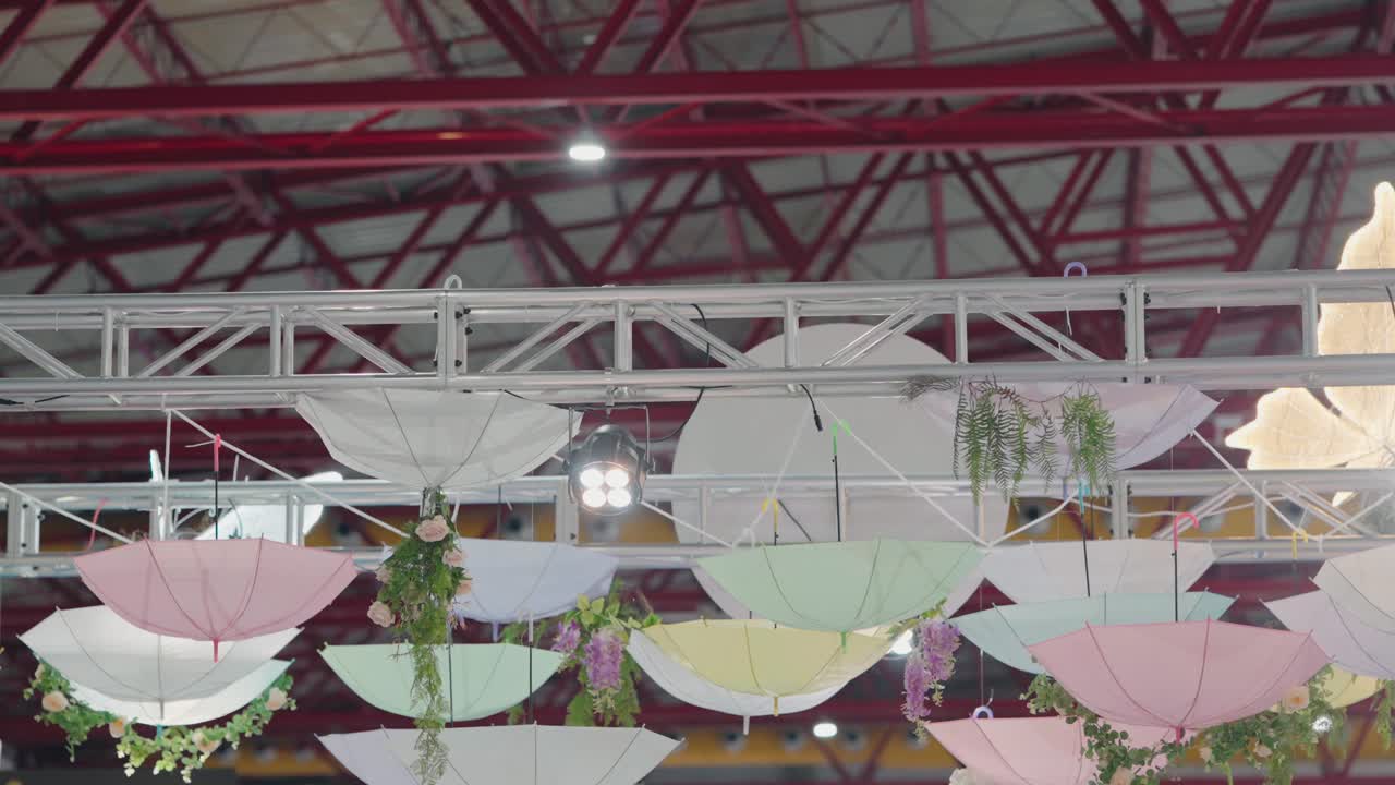 파스텔 색조의 거꾸로 된 우산이 천장에 매달려 있으며, 신선한 꽃으로 장식되어 기발한 이벤트 장식을 제공합니다.
