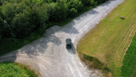 cinematic aerial drone camera footage you can see black jeep driving off-road in countryside landscape surrounded by green fields