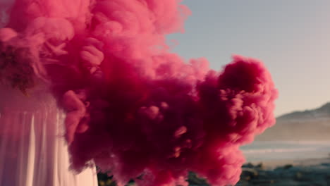 woman-holding-pink-smoke-bomb-on-beach-at-sunrise