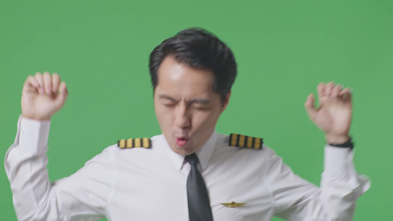 녹색 스크린 배경 스튜디오에 서서 춤을 추고 축하하는 아시아 남성 조종사의 클로즈업