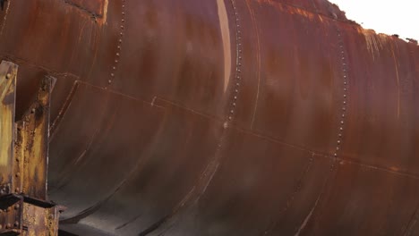 a close-up reveals the weathered surface of a reddish-brown rusted metal pipe with a cloud of snow floating around it