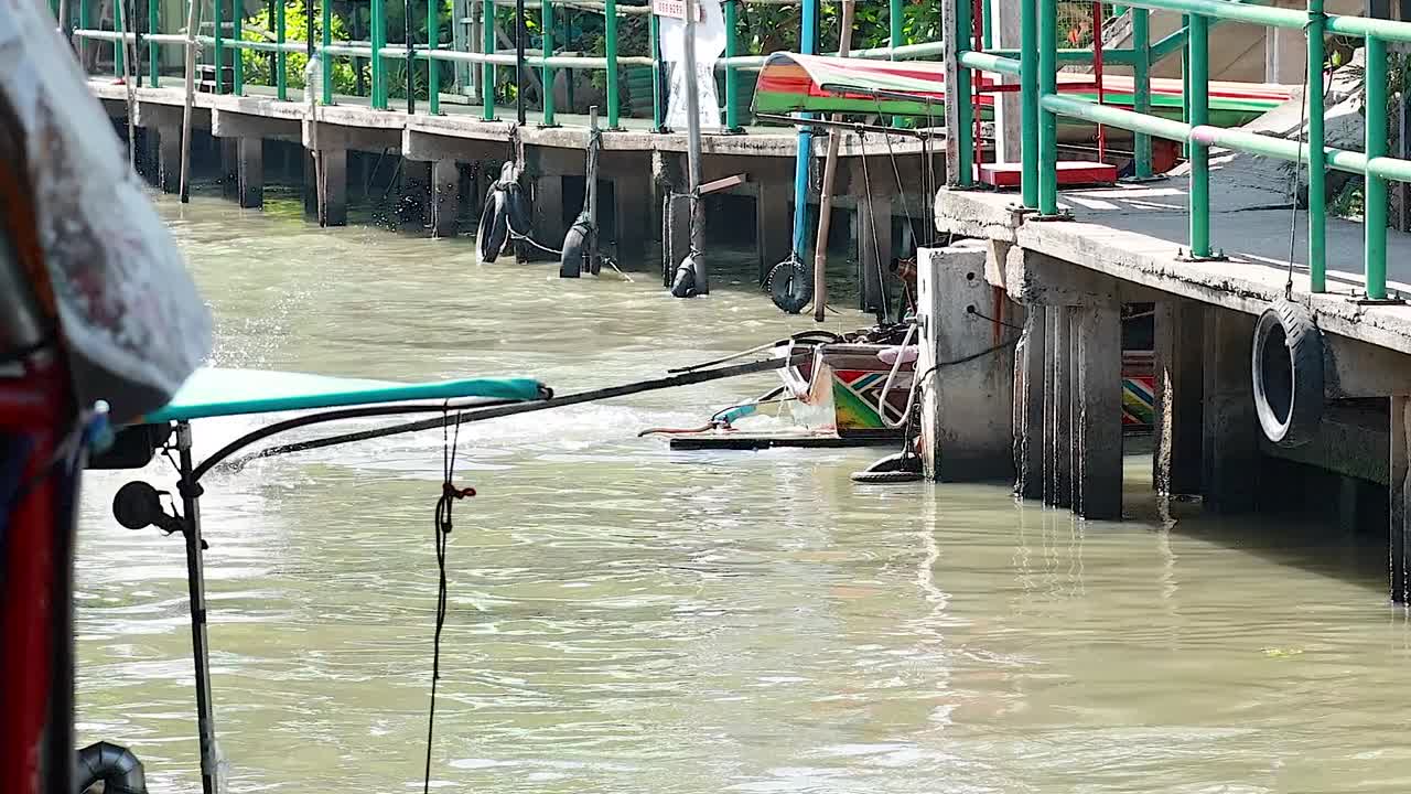 A vibrant boat maneuvers through a narrow canal beside a dock with green railings.