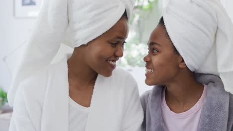 Happy-african-american-mother-and-daughter-wearing-towels-on-head-smiling