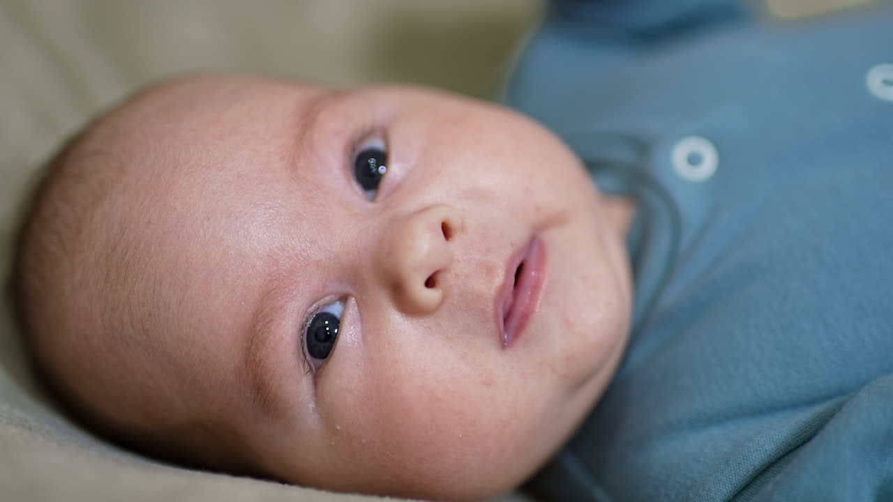 Adorable baby face portrait looking into camera. Sweet child lies on its back still at the grey background. Close up.