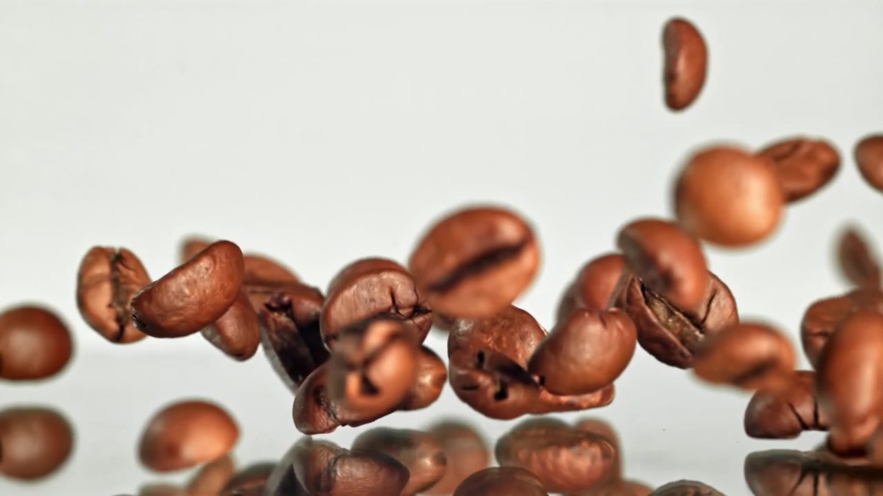 Chicchi di caffè che cadono al rallentatore su sfondo bianco