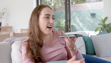 mujer caucásica feliz acostada en el sofá y hablando en el teléfono inteligente en cámara lenta