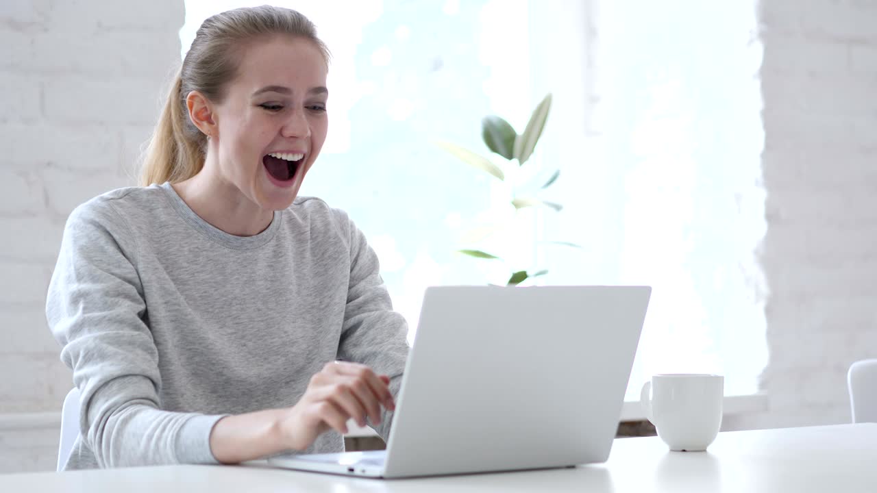노트북에서 일하는 흥분한 젊은 여성이 성공을 축하하고 있습니다.