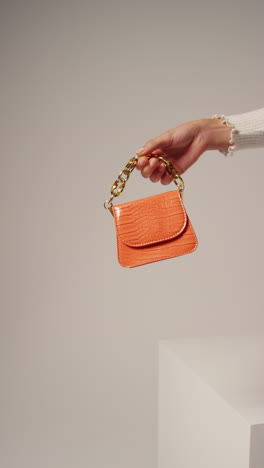 close up vertical video of female social media influencer producing user generated content holding out orange fashion handbag