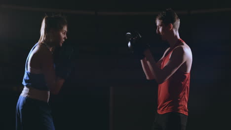 beautiful brunette boxer working out blows to the paws with a trainer in a dark room