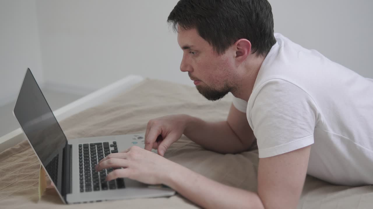 남자가 침대에 노트북을 가지고 일하고 있다.