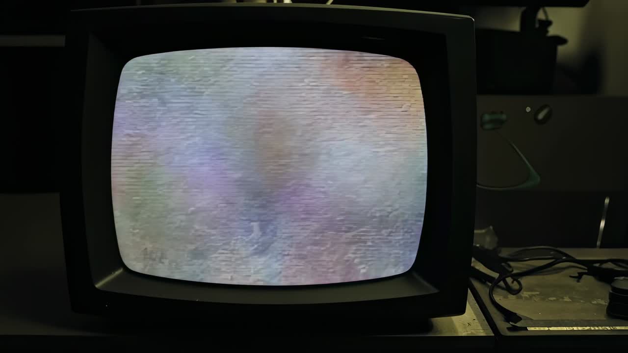 Flickering cathode-ray television displaying shifting static hues in workshop, power cables, module