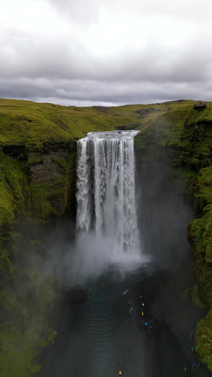 4K cinematic drone footage of Skógafoss Waterfall in Iceland, capturing the immense curtain of water cascading from towering cliffs surrounded by lush green landscapes. Iceland_12