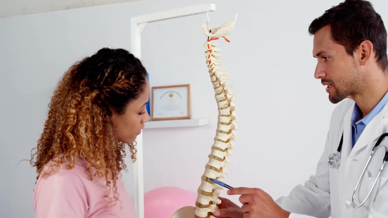 fisioterapeuta explicando el modelo de la columna vertebral al paciente