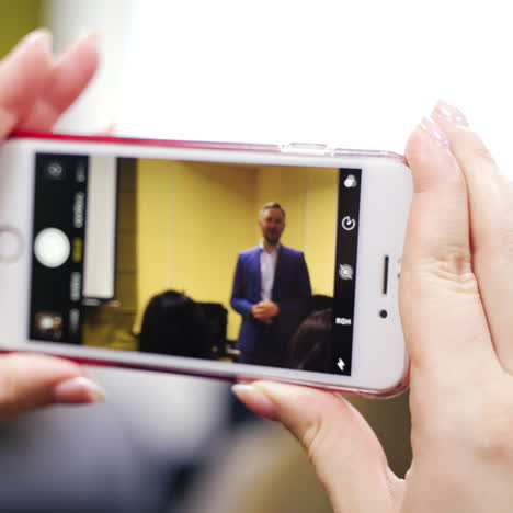 smartphone in woman's hands during seminar. woman is recording the video of the male speaker on her phone at conference indoors. close-up.