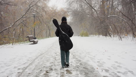 back view of a person walking through a snowy park path, carrying a guitar pack, with frosted bare trees and benches along the way, creating a serene winter scene