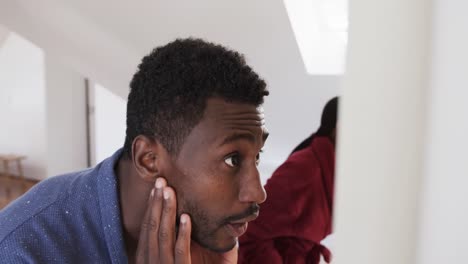 African-american-couple-using-face-cream-and-looking-in-bathroom-mirror-in-the-morning,-slow-motion