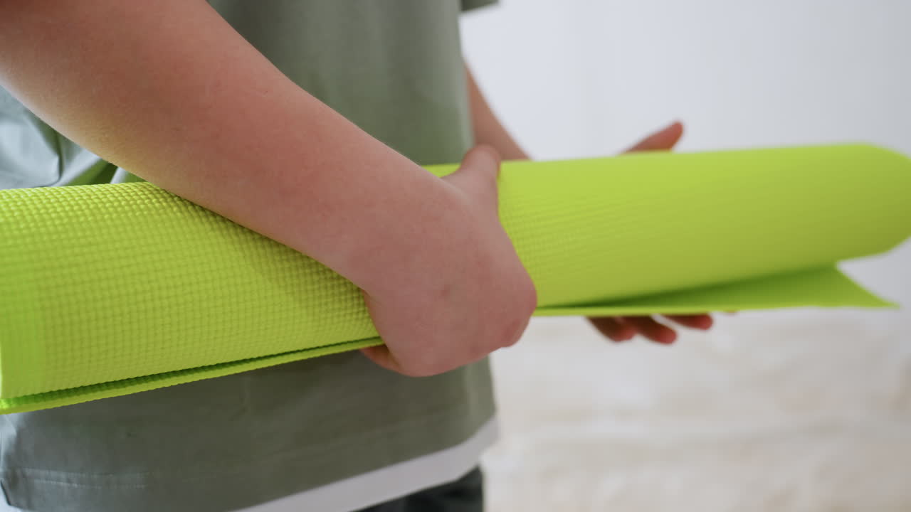 Close up of kid carefully folding bright green exercise mat inside cozy home, soft daylight highlights calm atmosphere, focused hands show responsibility