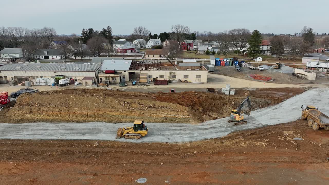 Heavy machinery operates at a construction site in a rural area, moving earth and preparing the land for future development and infrastructure improvements.