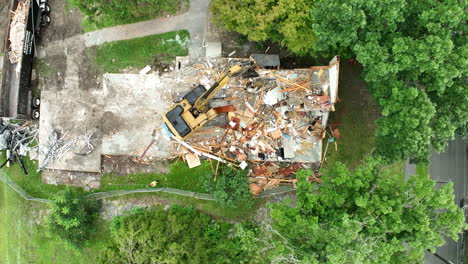 an excavator is dismantling an old house as part of the demolition process - aerial topdown shot