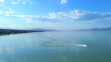 Vista-Aérea-De-Un-Jetski-Cabalgando-A-Alta-Velocidad-Tallando-A-Través-Del-Agua-En-El-Lago-Utah-Dejando-Rastros-De-Rocío-Blanco-En-Su-Camino---Jetski-Está-Cabalgando-Hacia-La-Cámara-Y-Desaparece-De-La-Vista