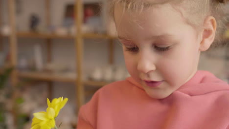 nahaufnahme eines blonden kleinen mädchens, das gelbe blumen in einer handwerkswerkstatt riecht