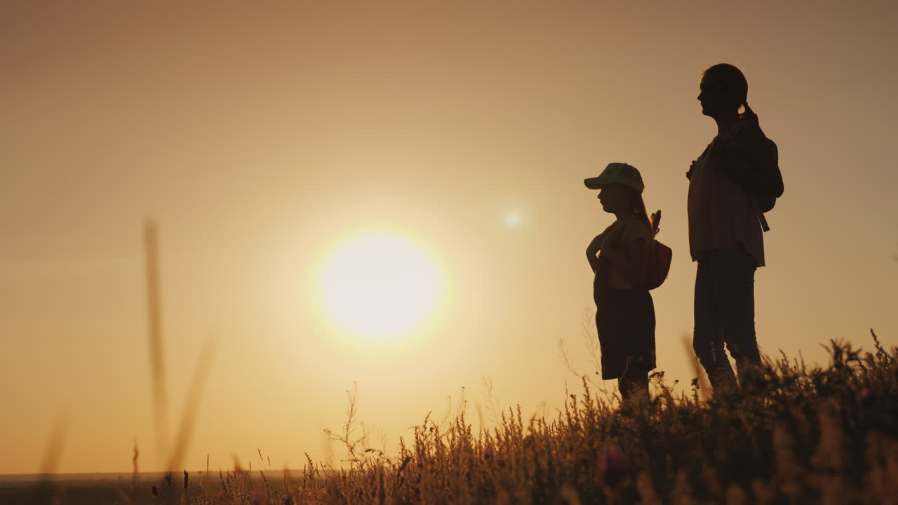 mamma e figlia stanno ammirando l'alba che stanno con gli zaini dietro la schiena in una foto
