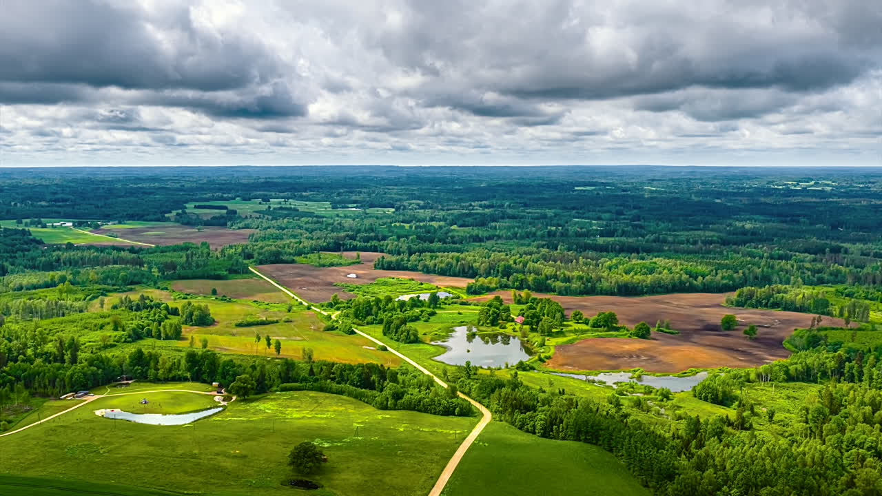Forested fields and hills with fast-moving clouds creating shadows over rural, panoramic high angle