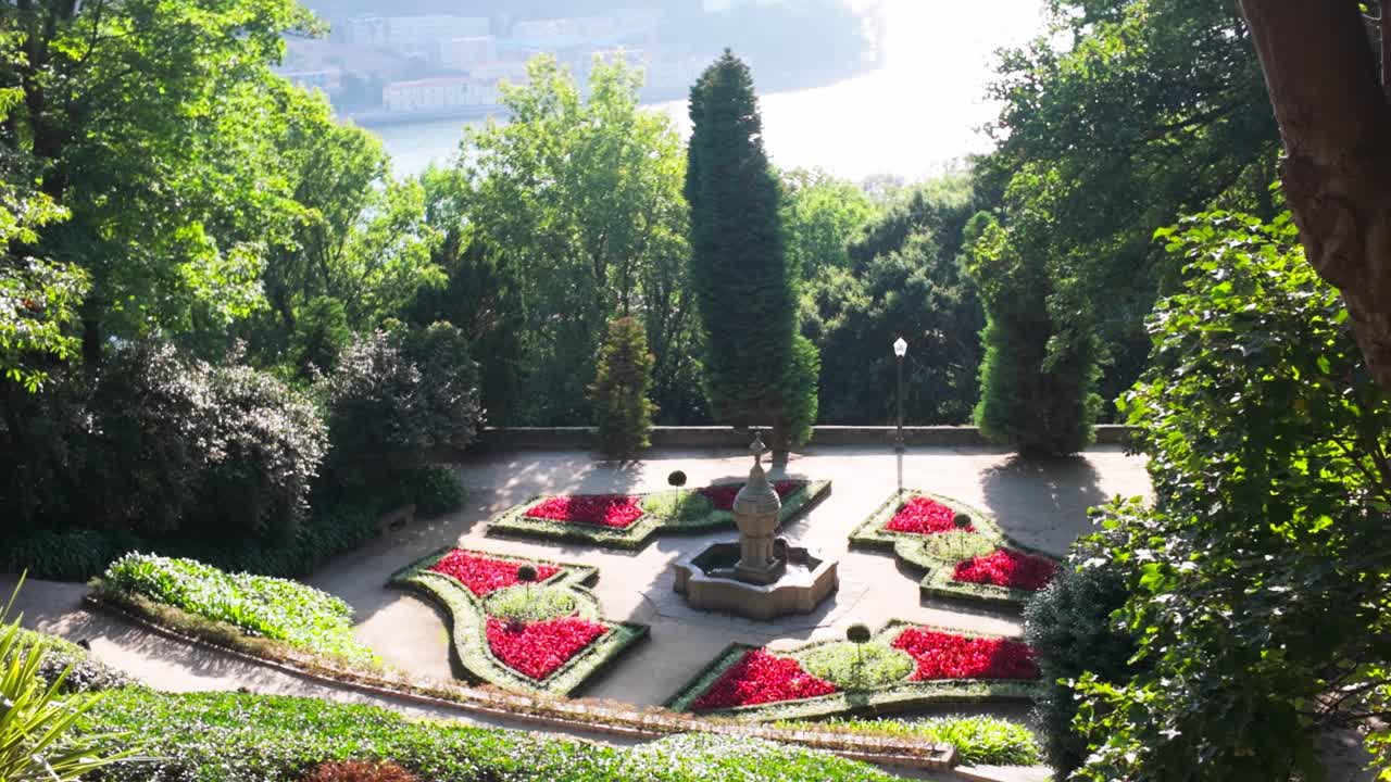 View of a vibrant garden with manicured flower beds and a fountain in Porto