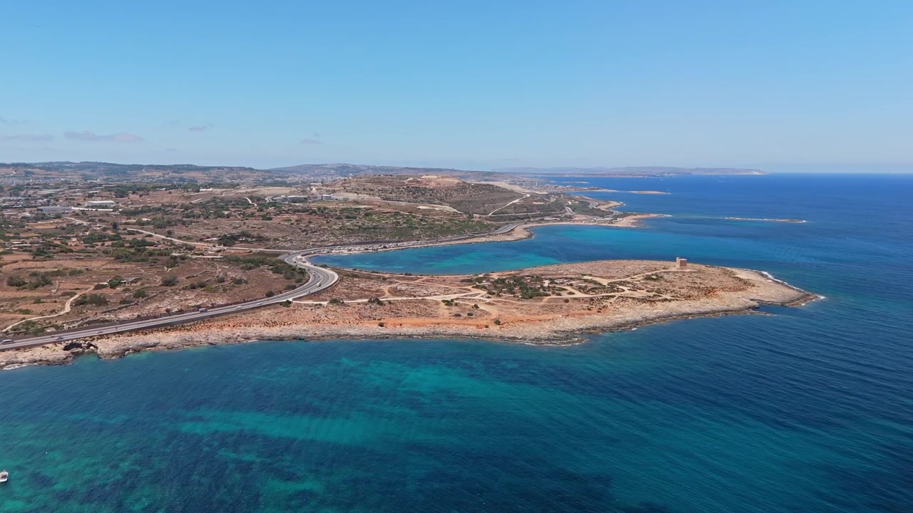 Costa di Naxxar, Malta, con litorale roccioso, torre di avvistamento e strada costiera lungo il Mar Mediterraneo in una soleggiata giornata estiva con acqua azzurra e limpida, vista aerea